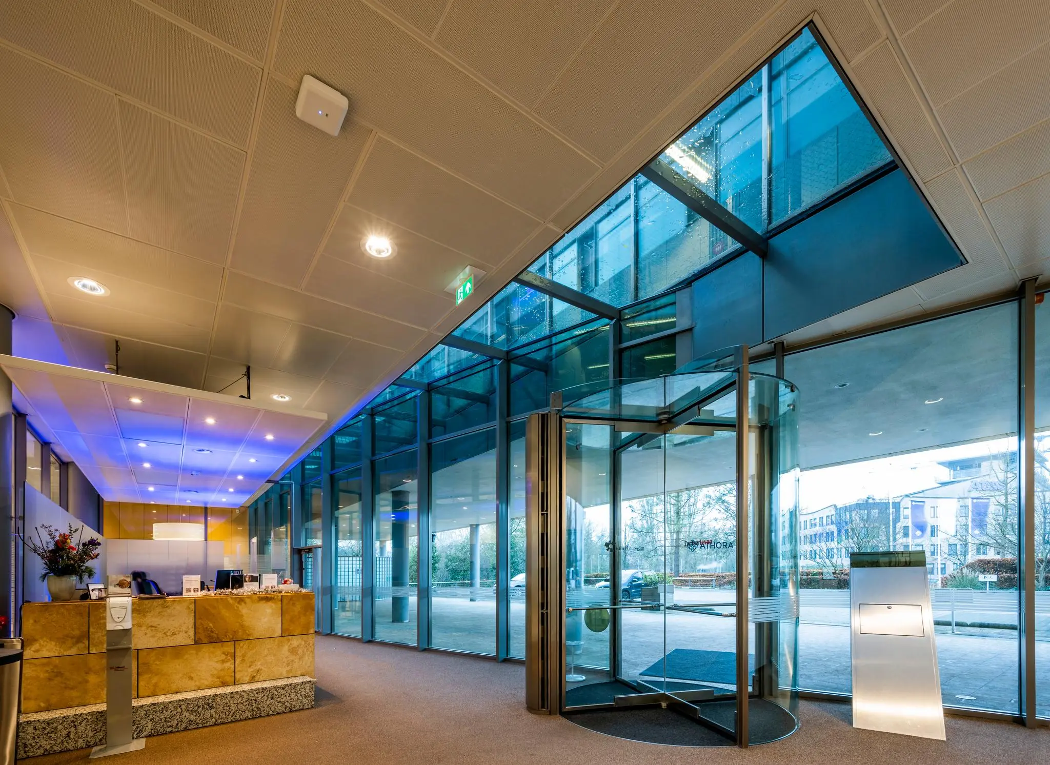 Moderne entreehal met glazen draaideur en receptiebalie aan de Burgemeester Rijnderslaan.